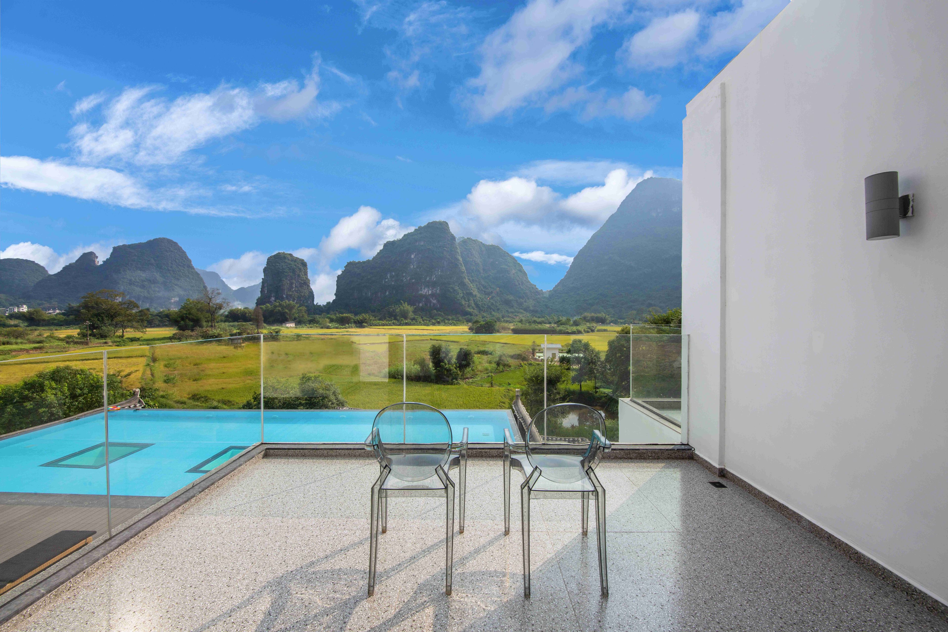 A balcony with a clear view of a swimming pool and mountains.