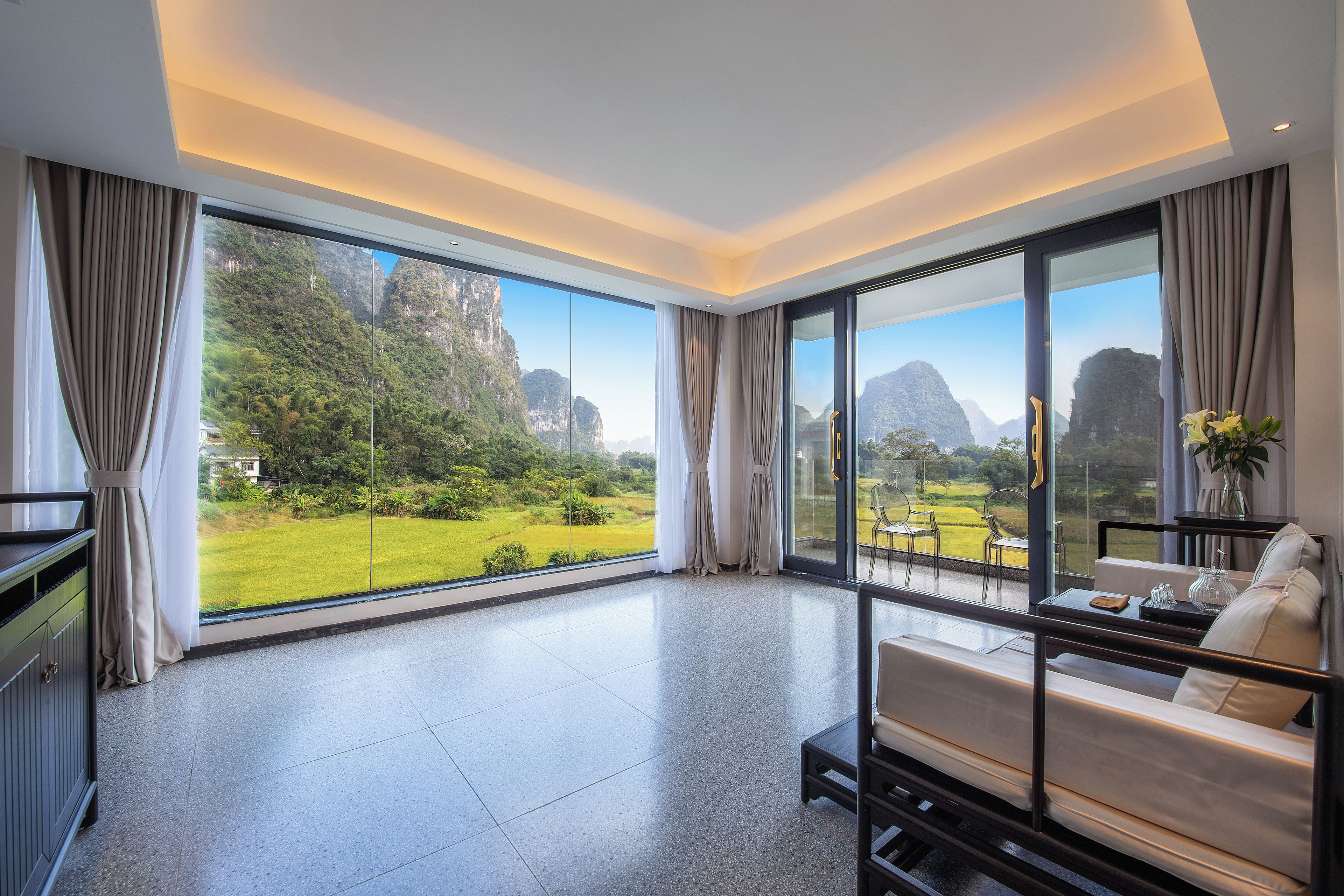 A spacious room with a large window offering a view of a lush garden and mountains.