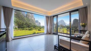 A spacious room with a large window offering a view of a lush garden and mountains.