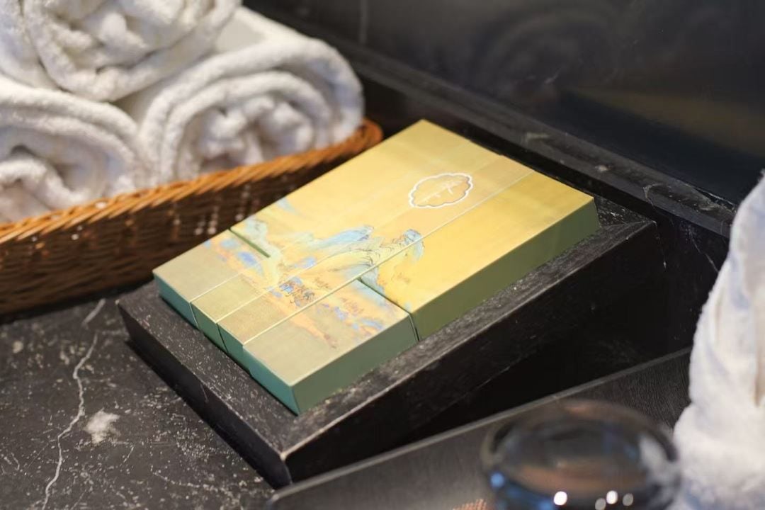 A set of neatly folded towels in a basket, a yellow box with a map design, and a glass of water on a marble surface.