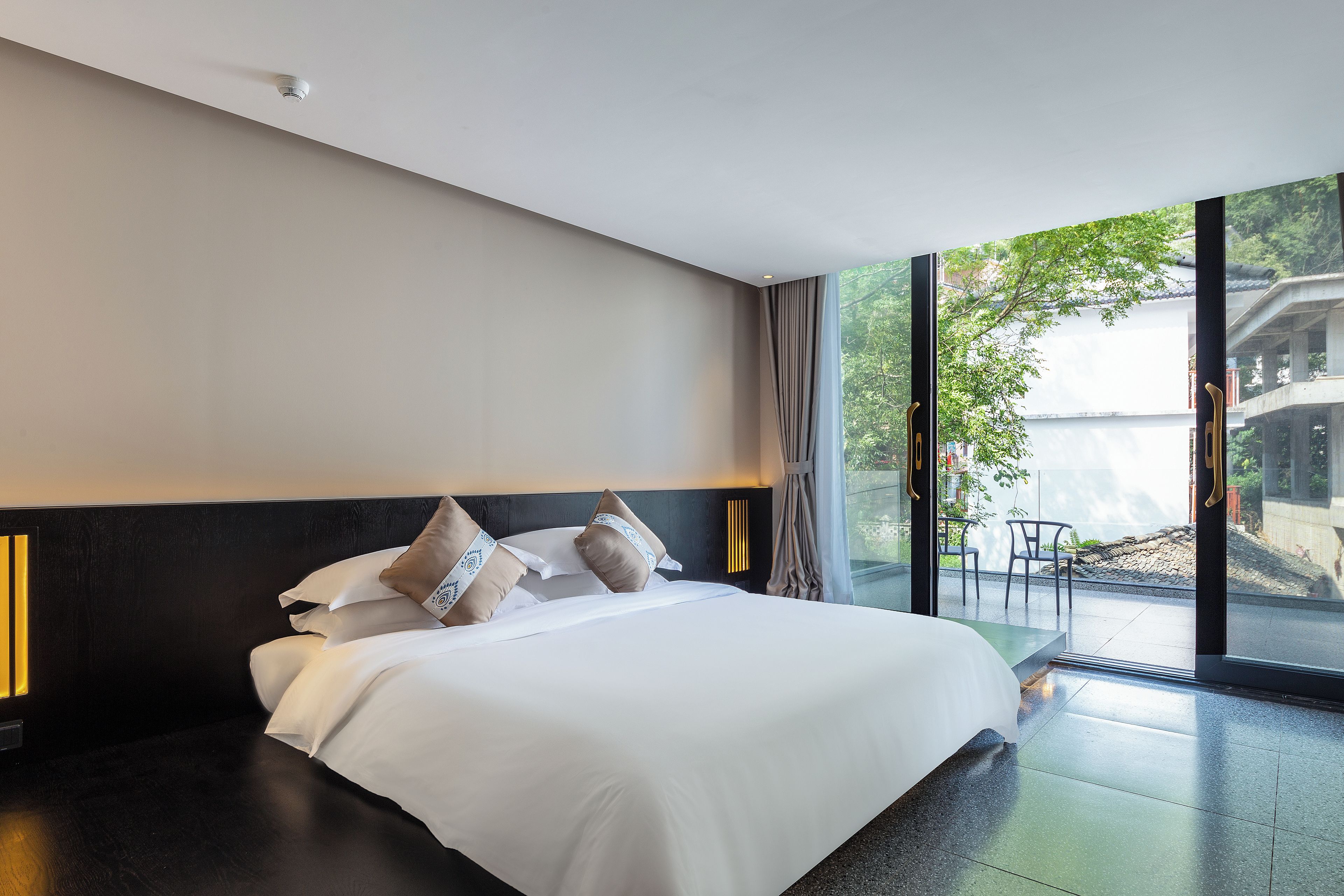 A modern hotel room with a large bed, a headboard, and a view of a building through the window.