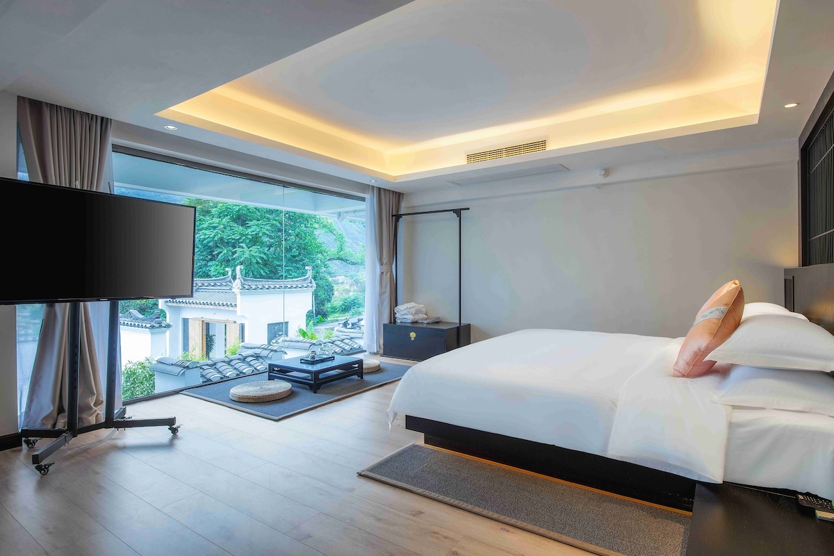 A modern bedroom with a large bed, a flat-screen TV, and a view of a traditional building.