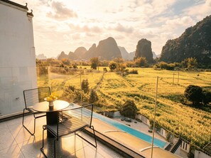 A terrace with a table and chairs, overlooking a pool and a landscape with fields and mountains. - Yangshou Mountain Vista Courtyard (Guilin)