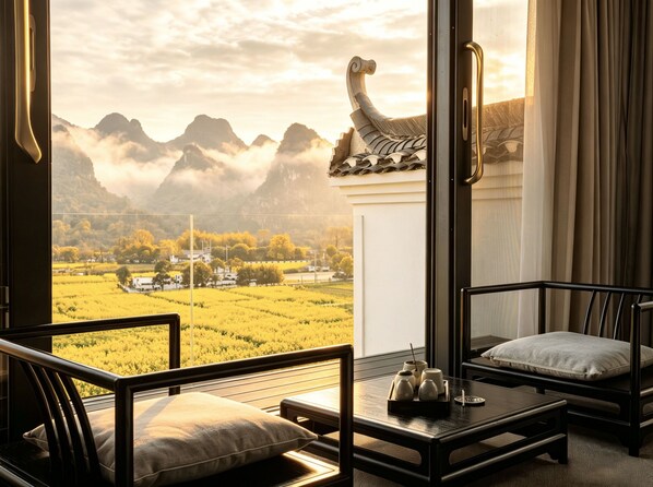 A room with a view of mountains and a field, furnished with a sofa and a table.
