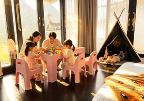 Una familia jugando con juguetes en una habitación con un ventanal grande, una cama y una estructura parecida a una tienda de campaña.
