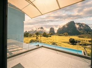 Un balcón con barandilla de vidrio que da a una piscina y un paisaje montañoso.