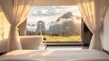 Une chambre avec un grand lit, une baignoire et une vue sur les montagnes par la fenêtre.