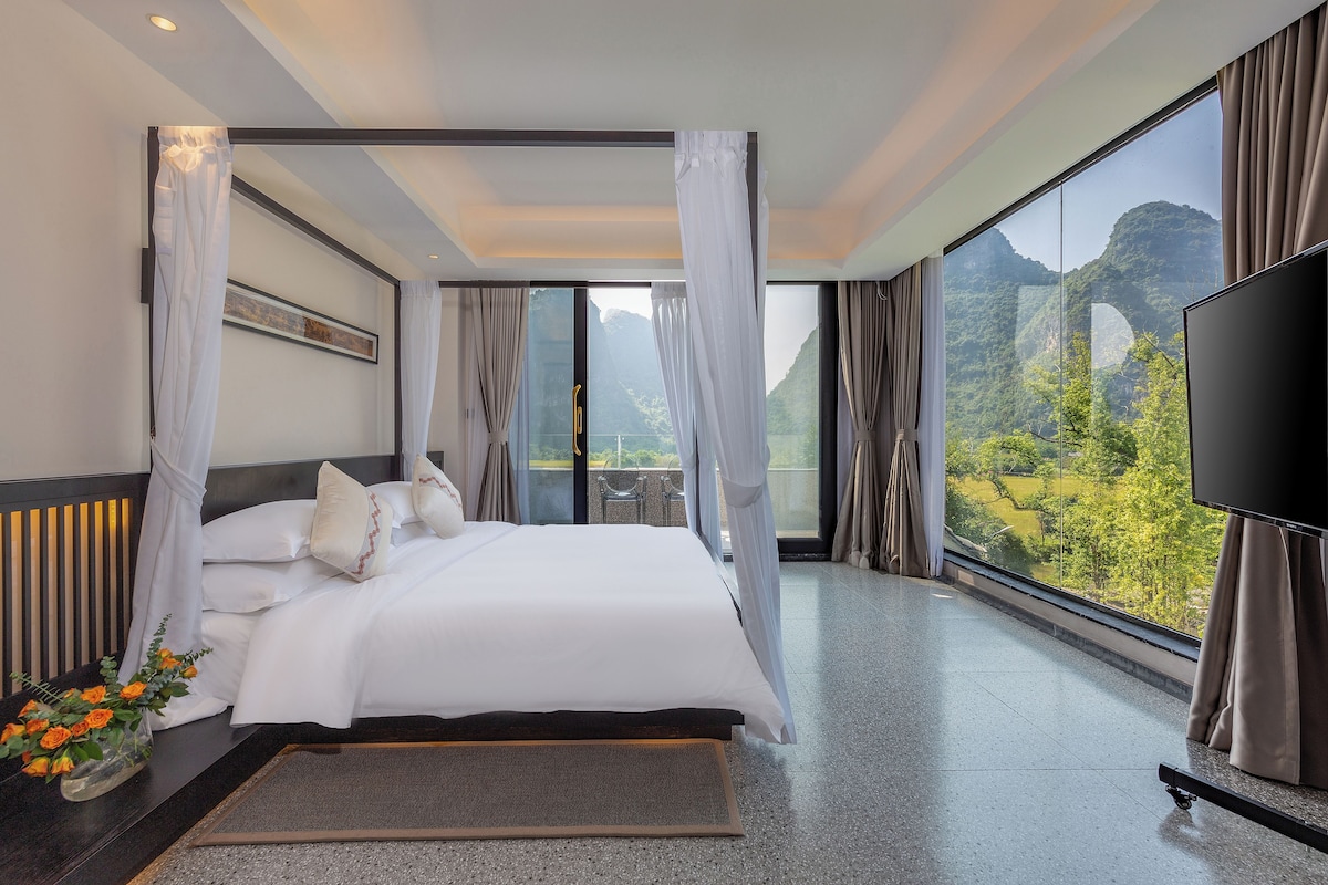 A modern hotel room with a large bed, a TV, and a scenic mountain view.