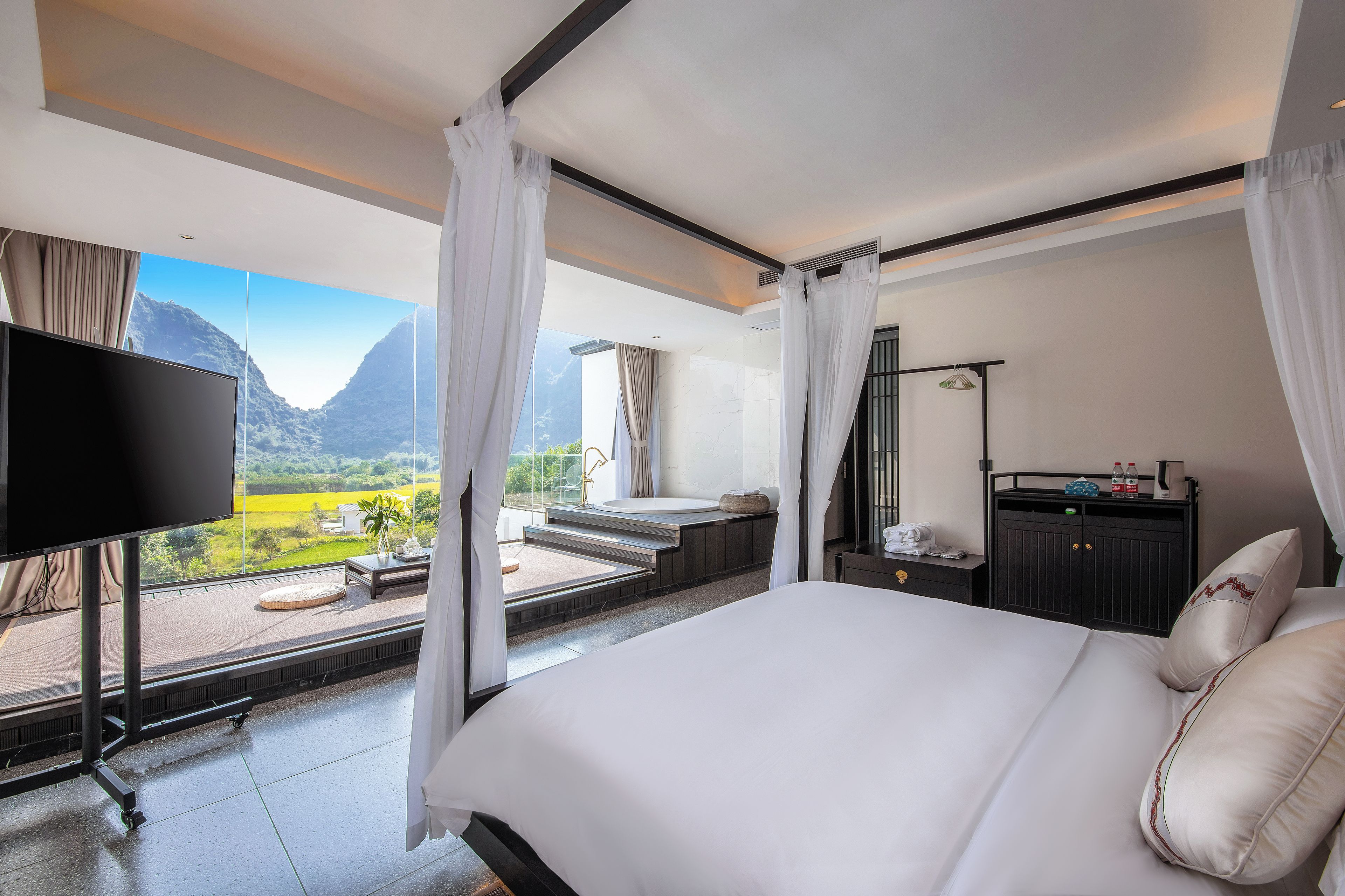 Habitación de hotel con una cama grande, televisión, baño con bañera y vista a un paisaje montañoso.