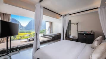 Habitación de hotel con una cama grande, televisión, baño con bañera y vista a un paisaje montañoso.