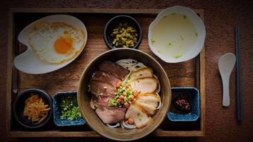A meal tray with a bowl of sliced meat garnished with green onions and peanuts, a fried egg, and various side dishes including noodles and a bowl of soup.