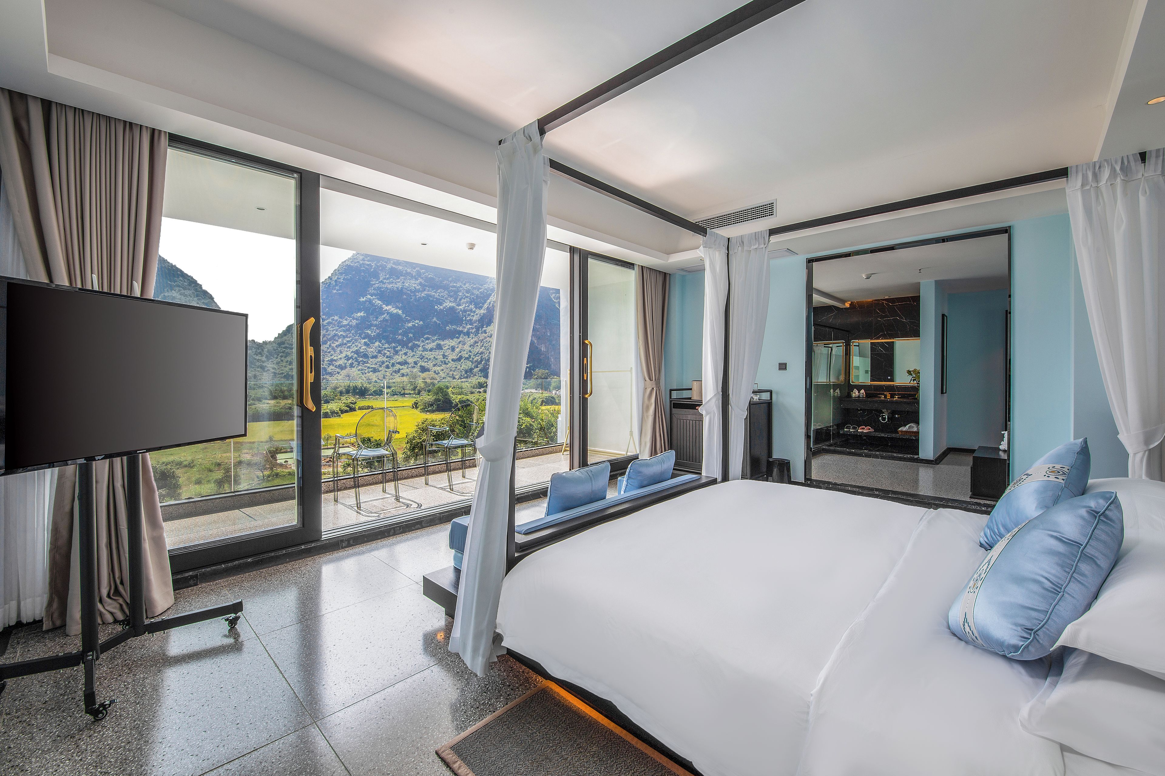 A hotel room with a large bed, a TV, and a balcony with a mountain view.