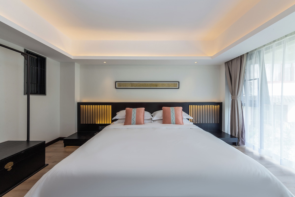 A modern hotel room with a large bed, a headboard with vertical slats, a bedside table, and a wall-mounted artwork.