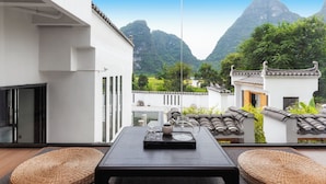 A balcony with a table set for two, overlooking a mountainous landscape and traditional architecture. - Yangshou Mountain Vista Courtyard (Guilin)