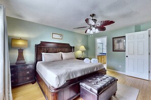 Ein Schlafzimmer mit einem hölzernen Bett, einer Bank, einem Deckenventilator und einem Nachttisch mit Lampe.