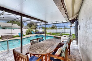 A covered outdoor area with a pool, wooden furniture, and a patio. - Splash House at Indian Ridge | 4BR/2BA Kissimmee | Pool, Game Room (Kissimmee)