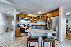 A kitchen with wooden cabinets, a stainless steel refrigerator, a microwave, and a large island with stools. - Splash House at Indian Ridge | 4BR/2BA Kissimmee | Pool, Game Room (Kissimmee)