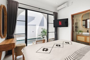 Ein Hotelzimmer mit Bett, Schreibtisch, Wandfernseher und einem Badezimmer mit Spiegel und Waschbecken.