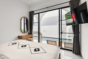 Ein modernes Schlafzimmer mit einem großen Bett, einem Fernseher, einem Spiegel und Blick auf einen Swimmingpool.