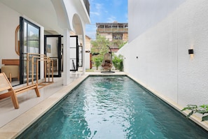 Ein Schwimmbecken mit freiem Blick auf die umliegende Architektur, darunter eine weiße Wand und ein Gebäude mit Balkon.
