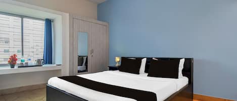 A hotel room with a bed, a window with curtains, a wardrobe, and an air conditioning unit.