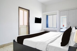Un dormitorio con una cama, un televisor montado en la pared, una puerta y una ventana con cortinas.