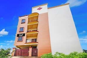 Un hôtel à plusieurs étages doté de balcons, une enseigne indiquant qu’il s’agit d’un hôtel géré par une entreprise, et une entrée sécurisée par un portail.