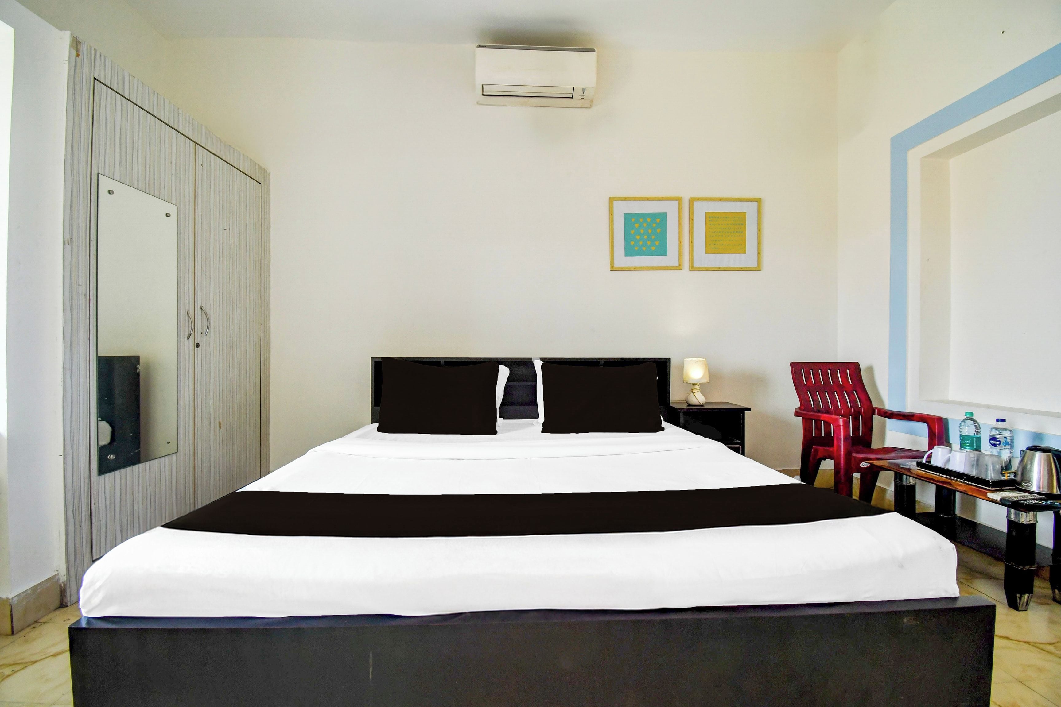 A hotel room with a bed, a wardrobe, a chair, a nightstand, and two framed pictures on the wall.