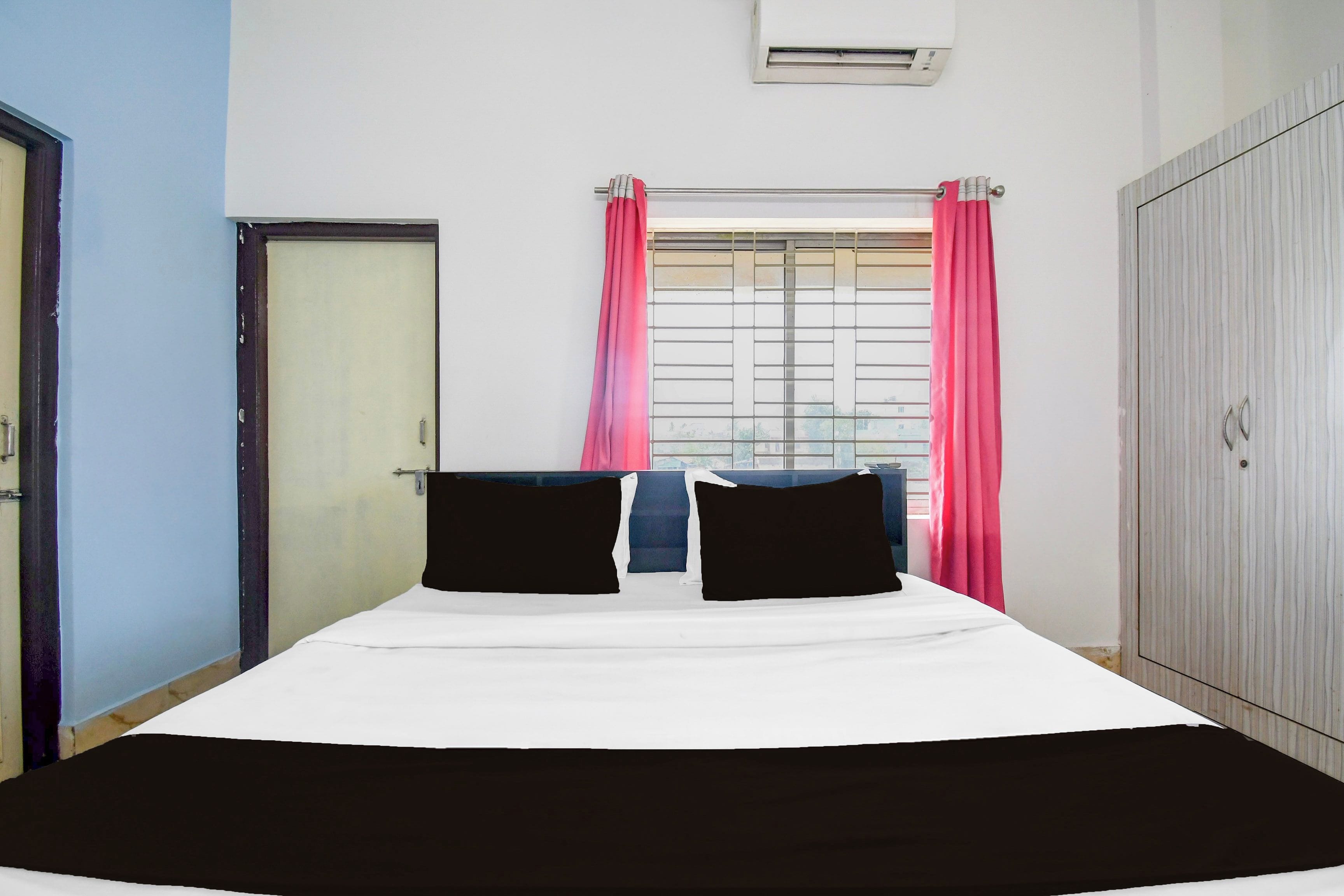 Una habitación con una cama, un armario, un ventanal con cortinas y un equipo de aire acondicionado.
