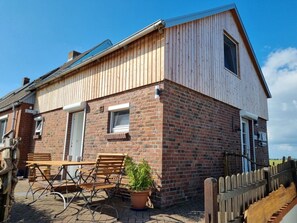Ein zweigeschossiges Haus mit Ziegelverkleidung, einem Holzanbau und einem eingezäunten Garten mit Gartenmöbeln.