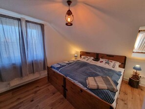 Ein Schlafzimmer mit einem hölzernen Bett, gestreifter Bettwäsche, einer Pendelleuchte und einem Fenster mit Vorhängen.