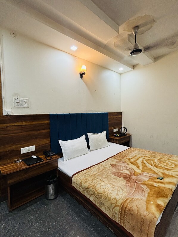 A hotel room with a bed, a nightstand, a wall-mounted lamp, a ceiling fan, and a power outlet.