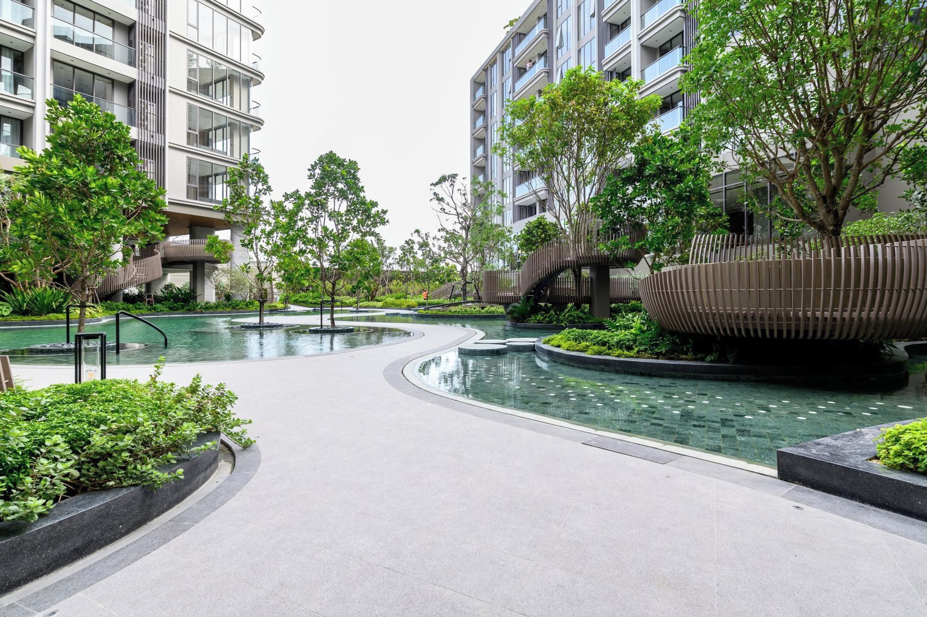 Un moderno complejo residencial con una fuente central, rodeado de follaje y arquitectura contemporánea.