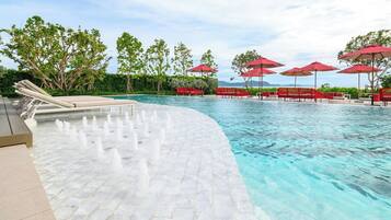 A pool area with a curved edge, lounge chairs, red umbrellas, and a clear view of the mountains in the background.