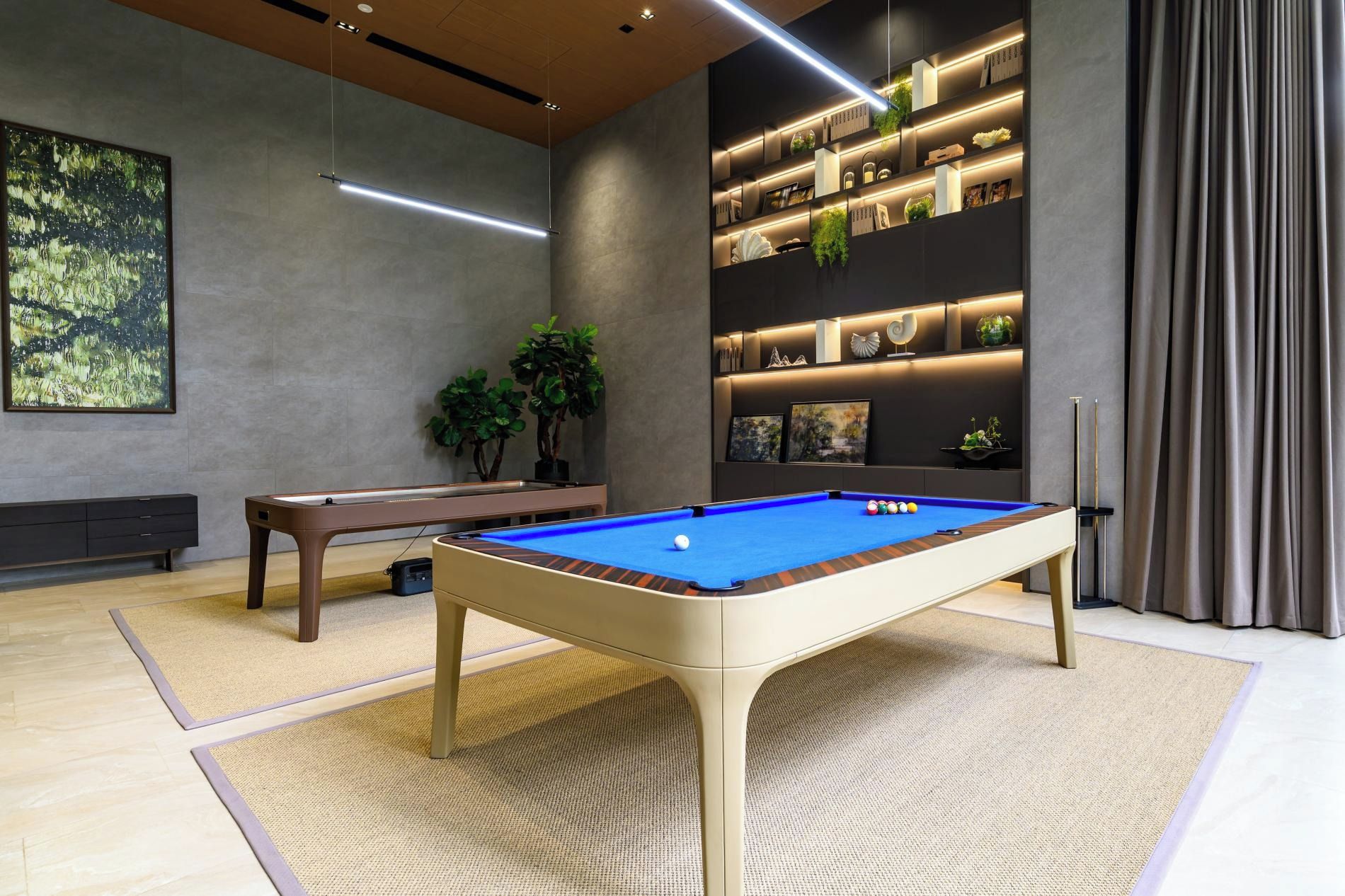 Una mesa de billar moderna en interior con superficie de fieltro azul, rodeada por una alfombra de tonos claros.