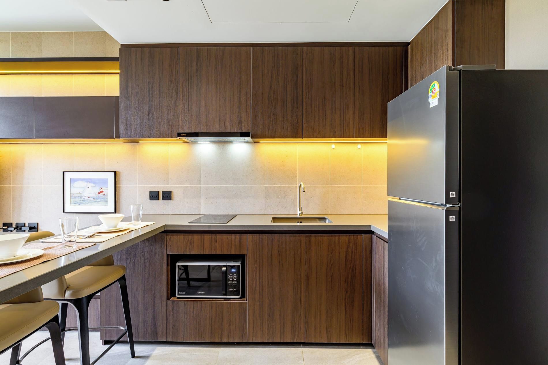 Una cocina moderna con microondas integrado, refrigerador de acero inoxidable y encimera de madera.