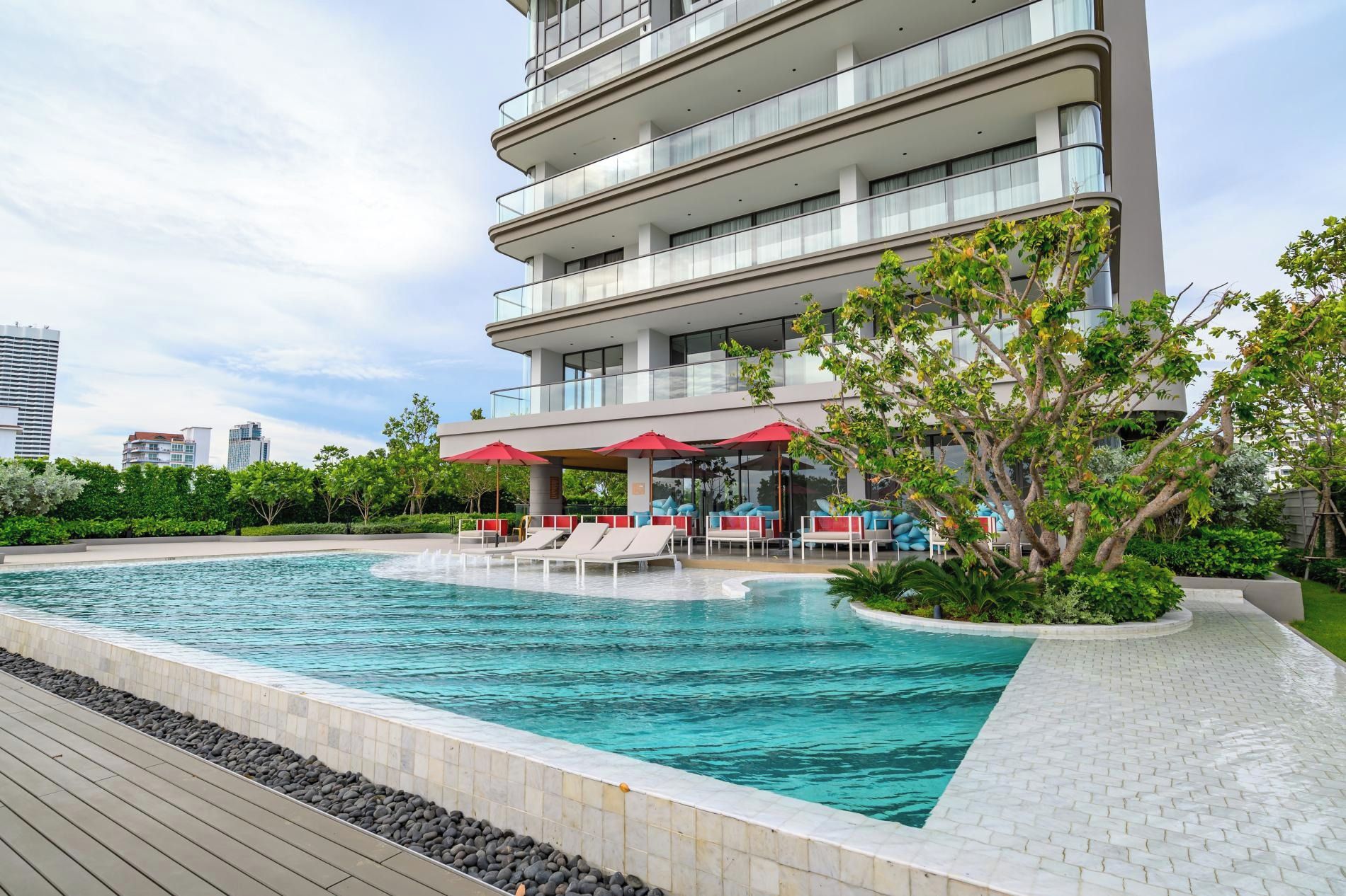 Un hotel moderno con piscina infinita en la azotea, asientos al aire libre y exuberante vegetación.