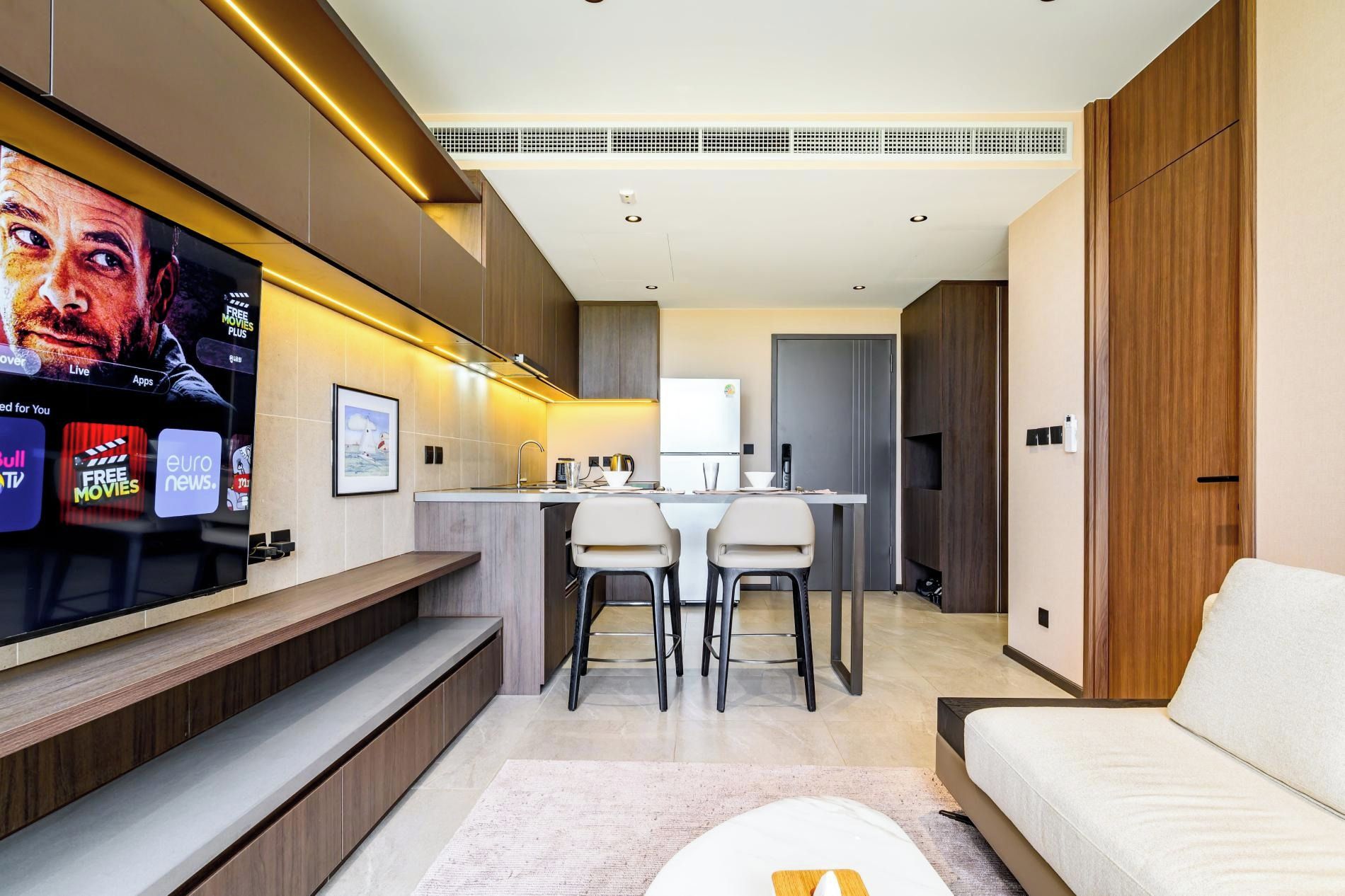 A modern living room with a flat-screen TV, a sofa, and a dining area with chairs.