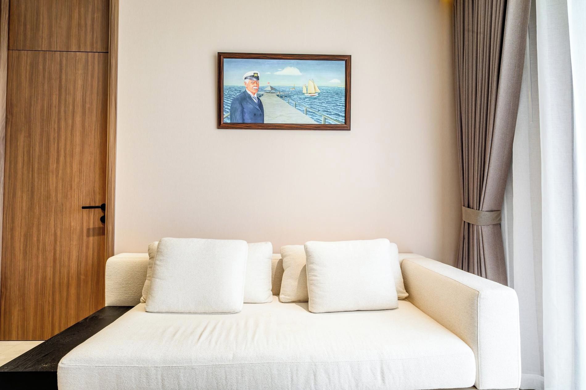 Una habitación de hotel con una cama, un armario de madera, un cuadro enmarco de una escena marina y una ventana con cortinas.