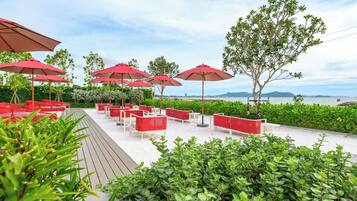 Sitzgelegenheiten im Freien mit Sonnenschirmen, ein Holzdeck und Blick aufs Meer.