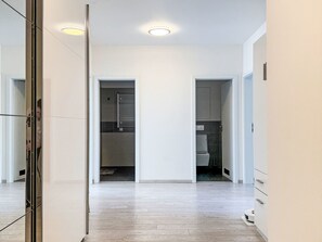 Un corridoio con pavimento in legno, una porta in vetro e vista su un bagno con il water e una doccia.