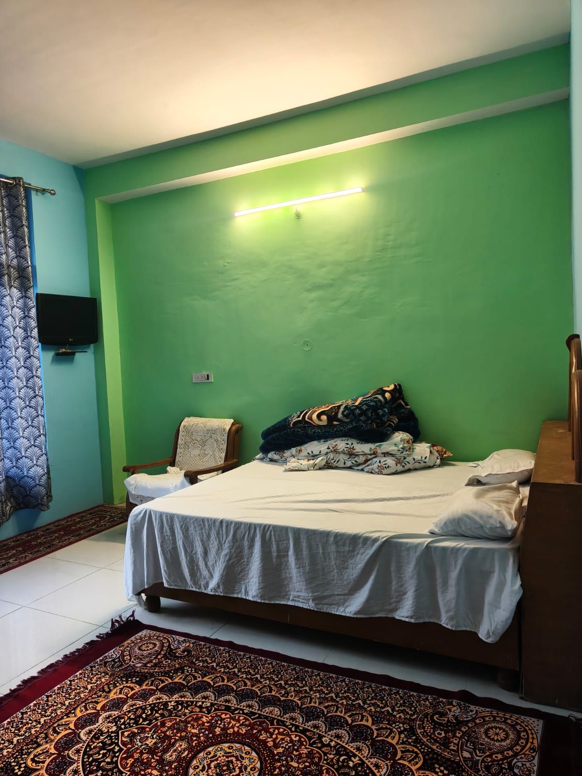 A room with a bed, a nightstand, a television, and a patterned rug.