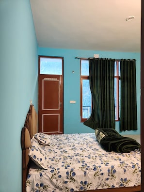 A bedroom with a bed, a window with curtains, a door, and a headboard. - The Raulane Homestay (Reckong Peo)
