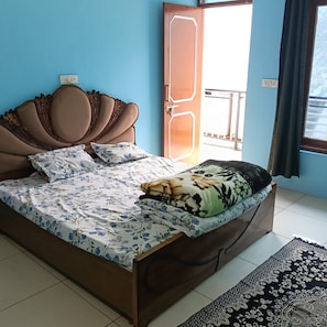 A bedroom with a wooden bed, floral bedding, a view of the outside, and a window with curtains. - The Raulane Homestay (Reckong Peo)
