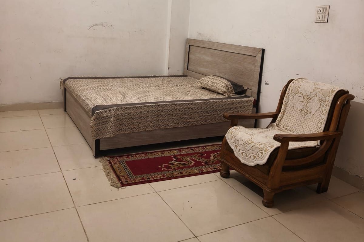 A bedroom with a bed, a chair, and a red patterned rug.