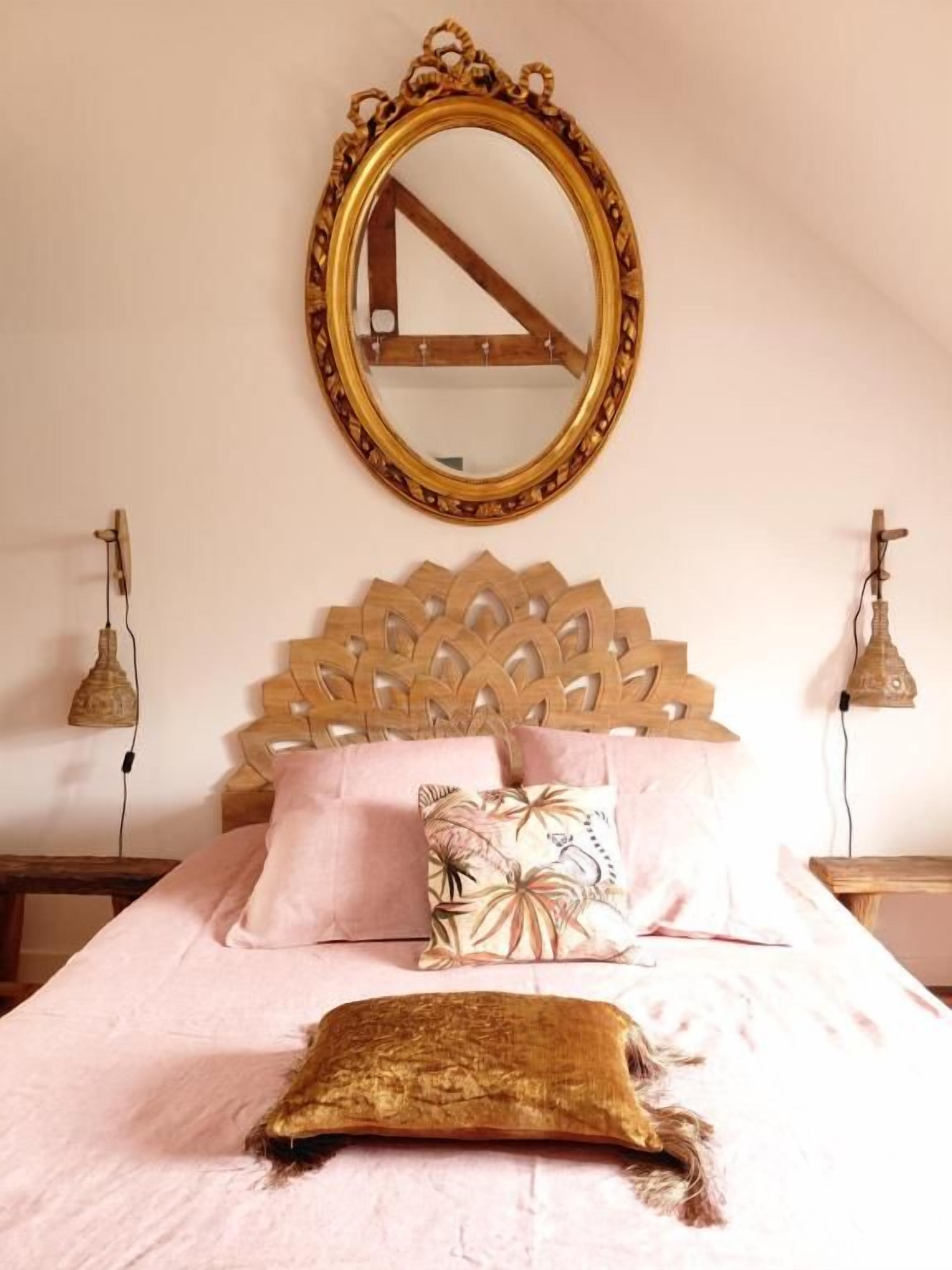 Une chambre à coucher avec une tête de lit en bois, un lit avec une literie rose, un coussin décoratif et un coussin d’ornement doré.