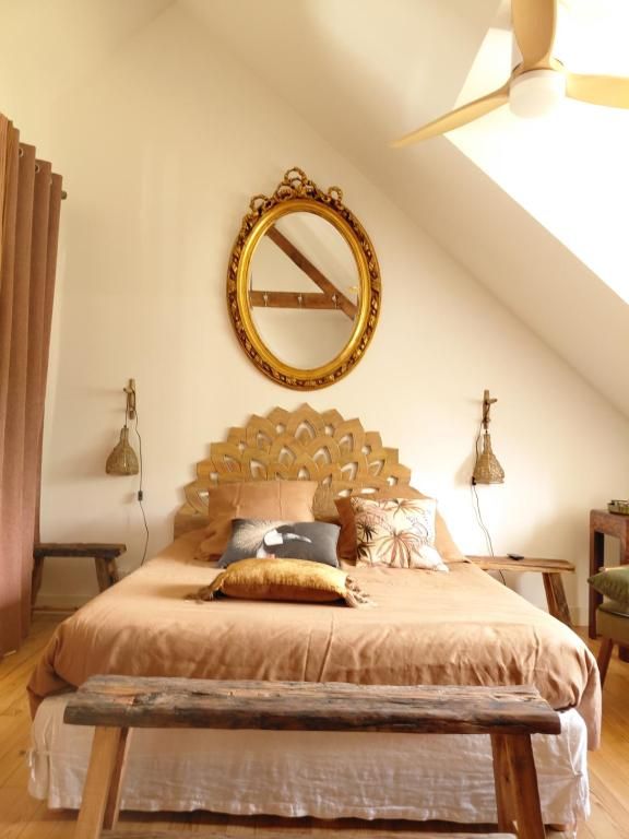 Une chambre avec un plafond en pente, un lit doté d’une tête de lit en bois, un miroir rond et deux lampes fixées au mur.