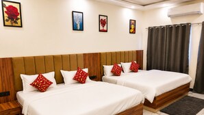 Habitación de hotel con dos camas, cabecero de madera, ropa de cama blanca, almohadas rojas estampadas, suelo de mármol y una obra de arte en la pared.