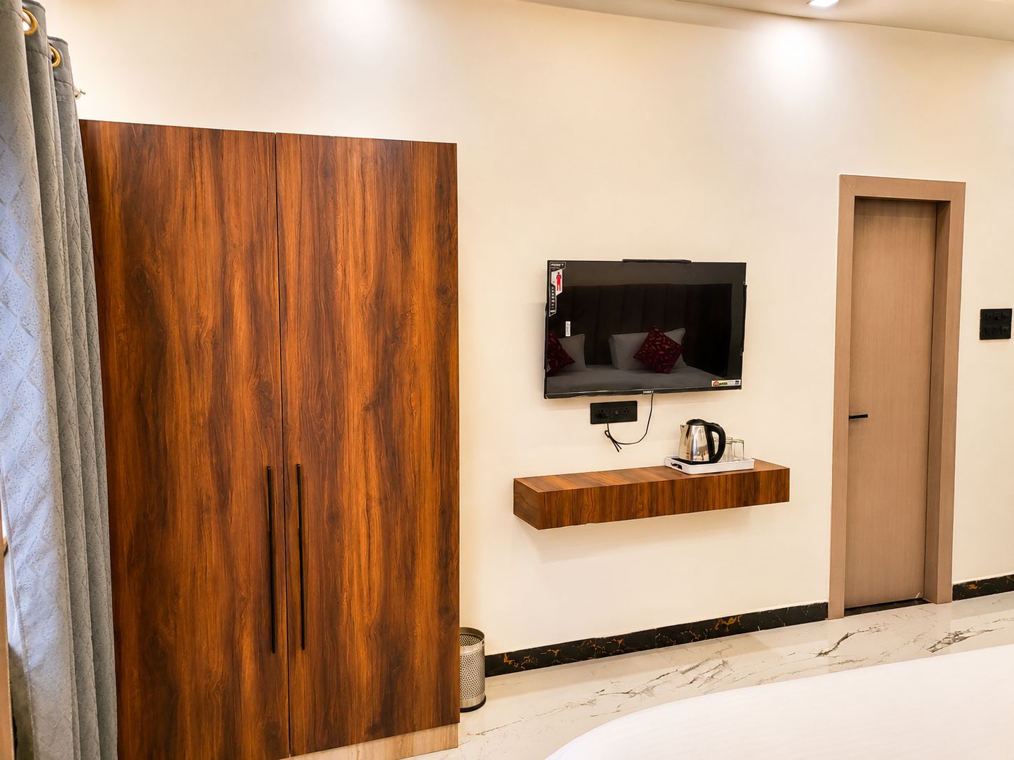 Een moderne kamer met een houten garderobe, een wandtelevisie, een koffiezetapparaat en een deur.