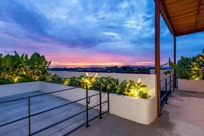 Eine Dachterrasse mit Blick auf die städtische Skyline in der Dämmerung, mit einer Holzpergola und Kübelpflanzen.